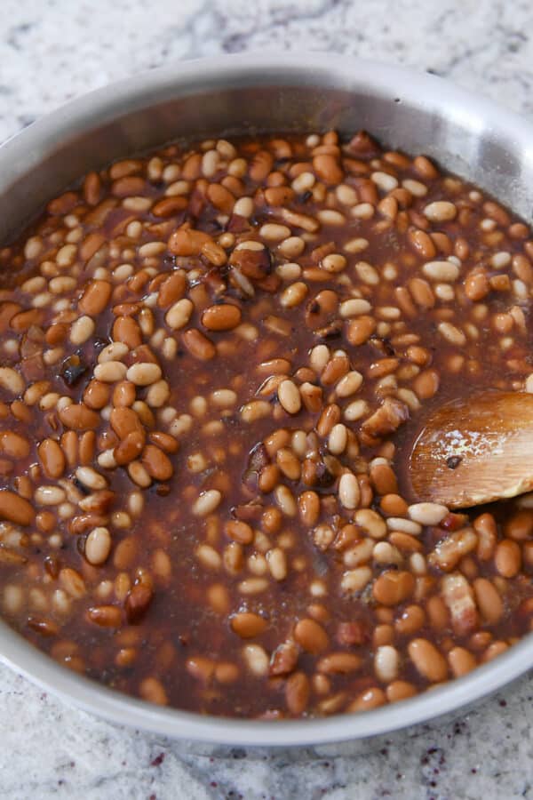 Baked beans in a shallow metal skillet with a wooden spoon