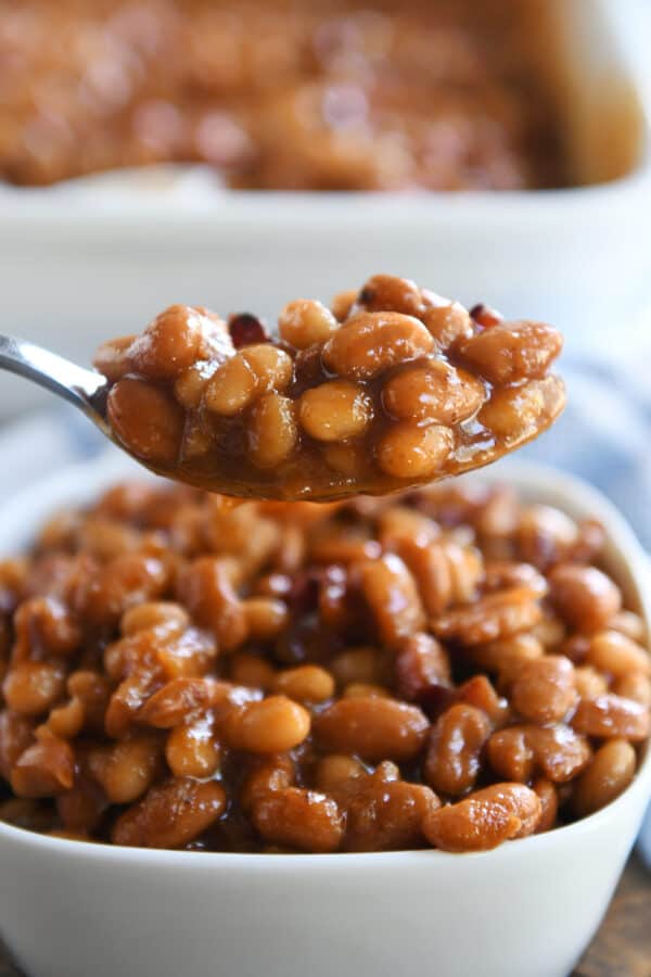 Spoonful of saucy baked beans over white square dish.