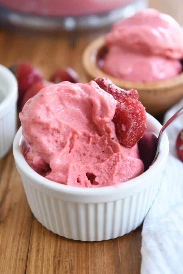 Half scoop of homemade strawberry frozen yogurt in white cup with silver spoon.