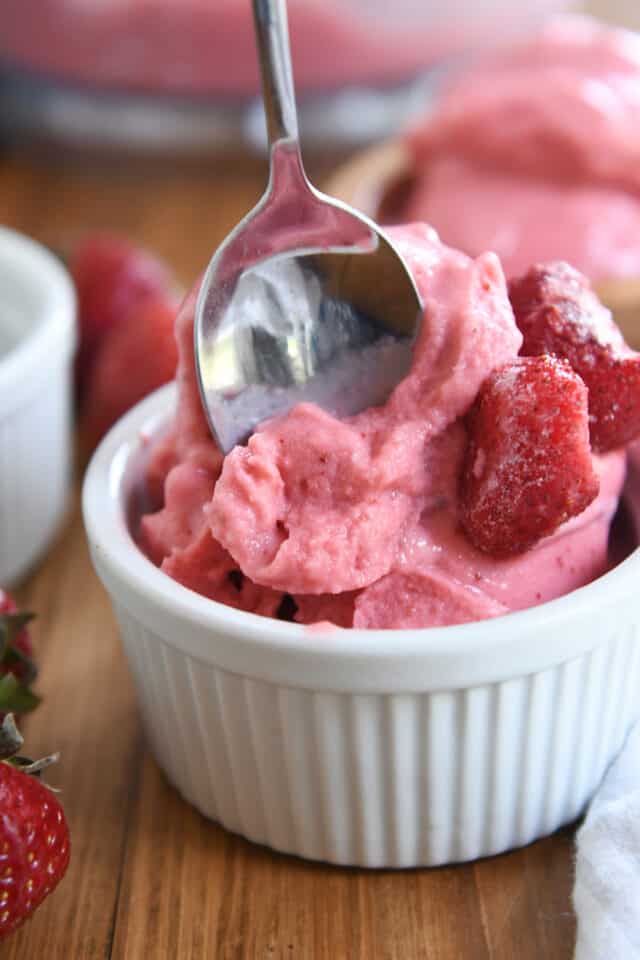 Spoon taking scoop of strawberry frozen yogurt in white cup.