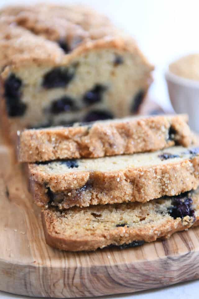 Three slices of blueberry muffin bread cut from the loaf on wood cutting board.