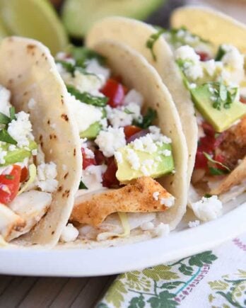 three fish tacos in corn tortillas on white platter