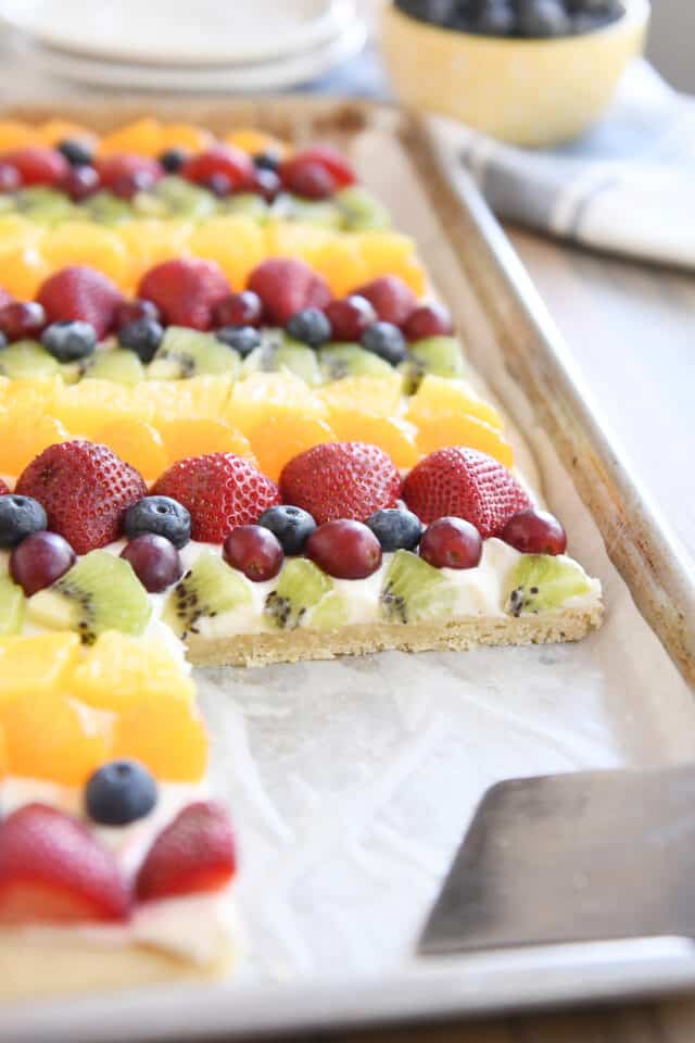 Sheet pan of fruit pizza with a serving taken out with metal spatula.