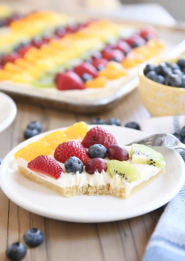 Square of the best fruit pizza with bite taken out on white plate.