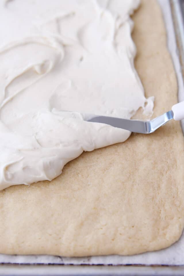 Spreading cream cheese frosting on sugar cookie crust for fruit pizza.