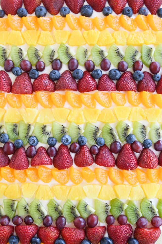 Rows of kiwi, red grapes, blueberries, strawberries, mandarin oranges and pineapple on fruit pizza.