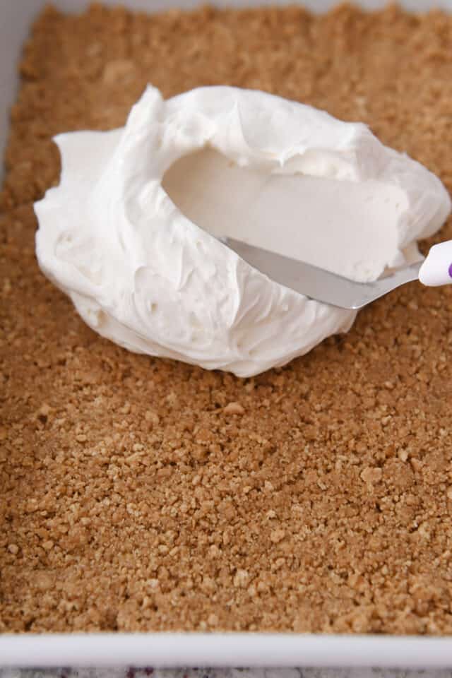 Spreading thick cream cheese cream on top of baked graham cracker crust.