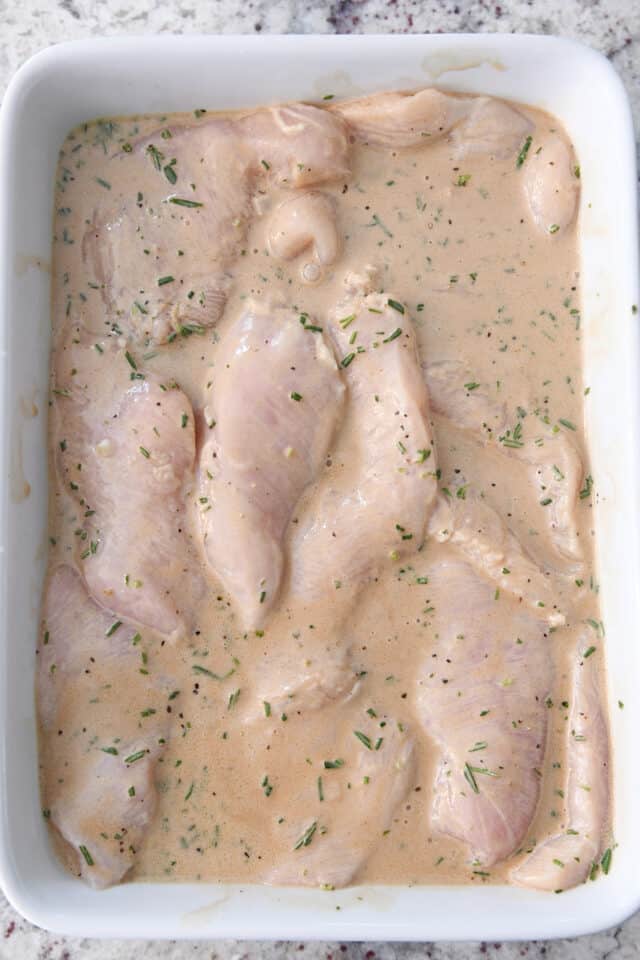Chicken breasts in rosemary ranch marinade in white pan.