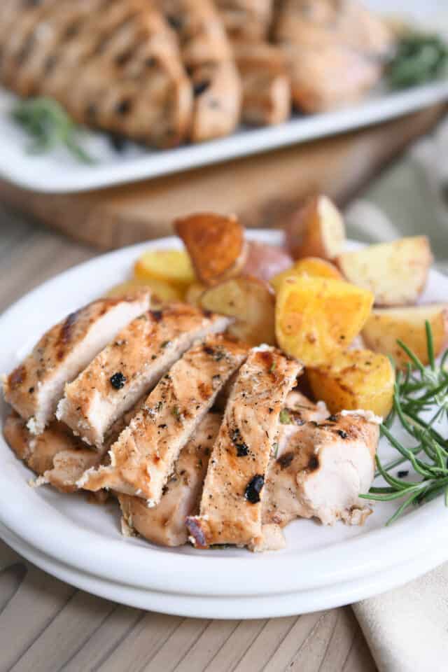 White plate with strips of grilled rosemary ranch chicken, fresh rosemary sprig and roasted potatoes.