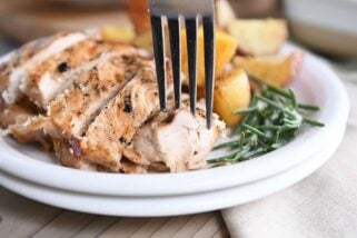 fork taking piece of rosemary ranch chicken on white plate with rosemary and potatoes