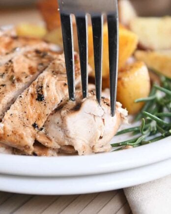 fork taking piece of rosemary ranch chicken on white plate with rosemary and potatoes