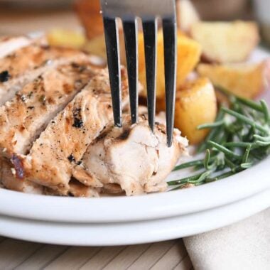 fork taking piece of rosemary ranch chicken on white plate with rosemary and potatoes