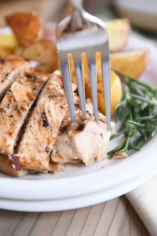 Fork taking piece of rosemary ranch chicken on white plate.