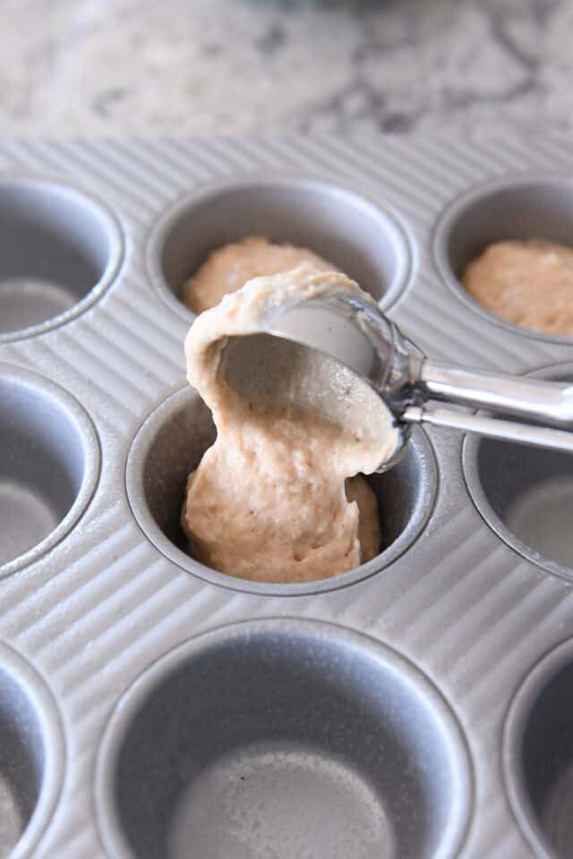 scooping muffin batter into greased muffin tin