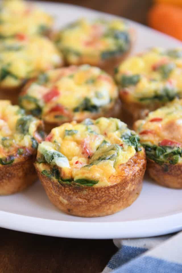 Six hash brown veggie egg cups on white platter with blue and white napkin.