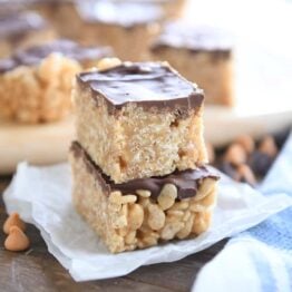 two scotcheroos stacked on white parchment with butterscotch and chocolate chips sprinkled around