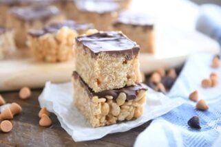 two scotcheroos stacked on white parchment with butterscotch and chocolate chips sprinkled around