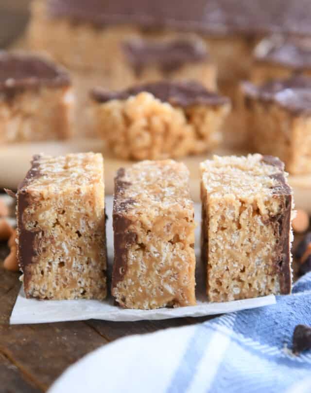 Three scotcheroo bars stacked side by side on white parchment paper.