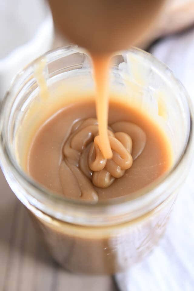 Drizzling thick butterscotch sauce in glass jar.