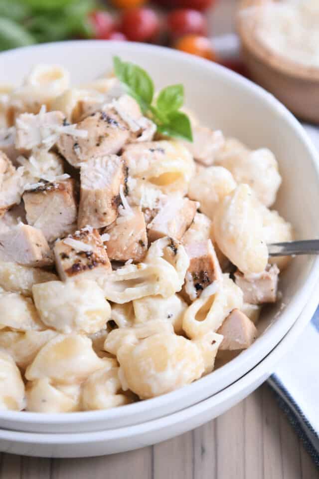 Grilled chicken on top of instant pot pasta alfredo shells in white bowl.