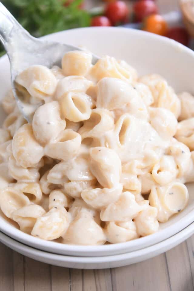Spooning helping of instant pot pasta alfredo in double stacked white bowls.