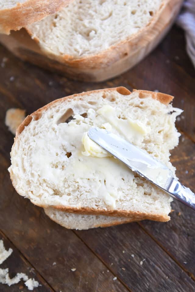 Spreading butter on half slice of no-knead peasant bread with butter knife.