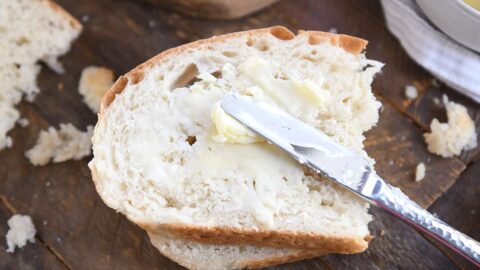 spreading butter on half slice of peasant bread with butter knife