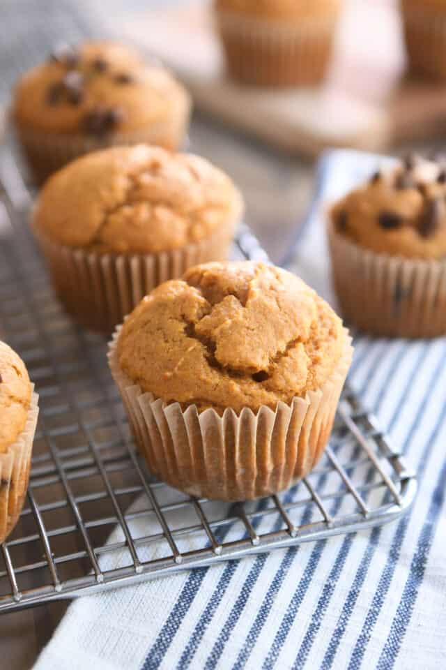 Sourdough pumpkin muffin in brown wrapper on metal cooling rack with three muffins in background.