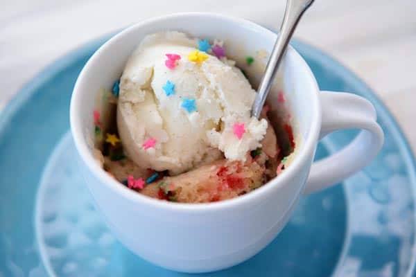 Top view of a mug filled with funfetti cake and a scoop of vanilla ice cream.