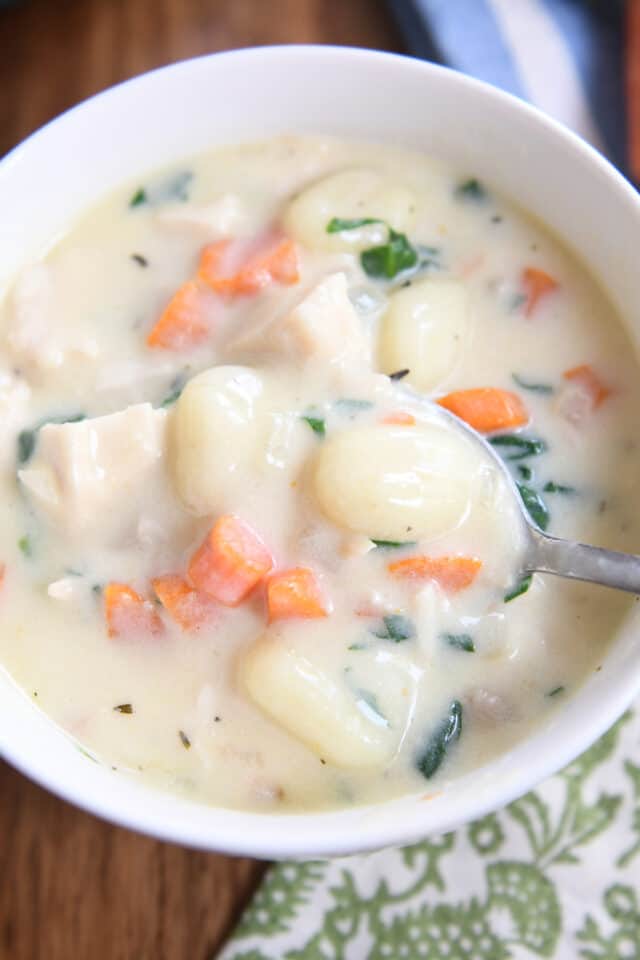 Top down view of creamy chicken gnocchi soup in white bowl with spoon.