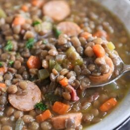 spoon lifting up small scoop of lentil soup in stone bowl