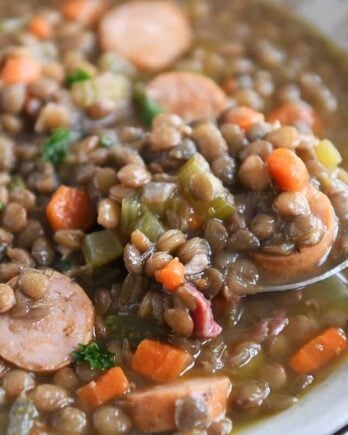 spoon lifting up small scoop of lentil soup in stone bowl