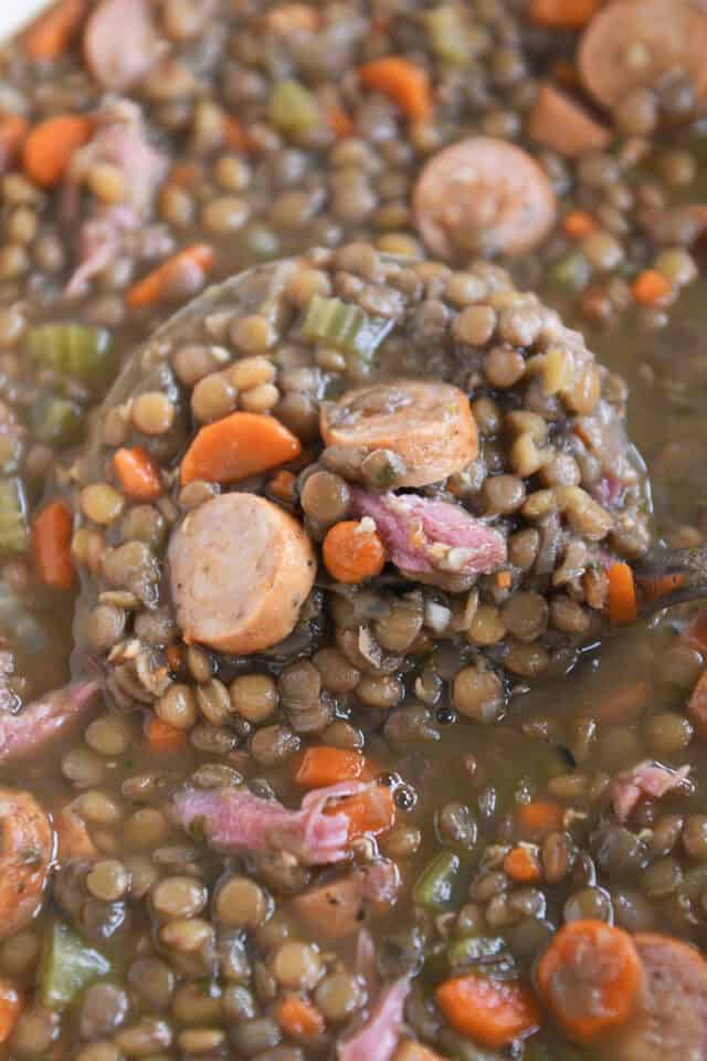 Ladle lifting up scoop of lentil soup with sausage and veggies.