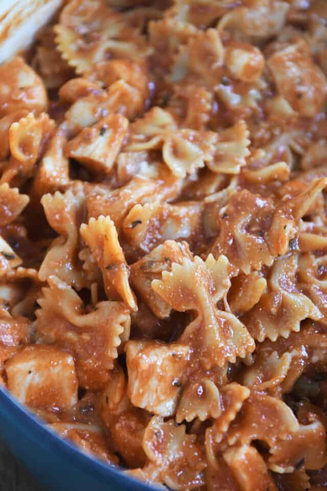 Cooked bowtie pasta and chicken in tomato sauce in blue pot.