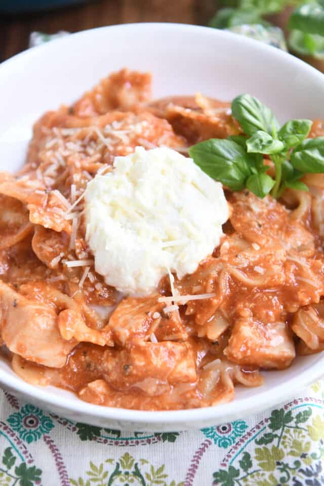 Serving of chicken lasagna in white bowl with spoonful of ricotta and fresh basil leaves.