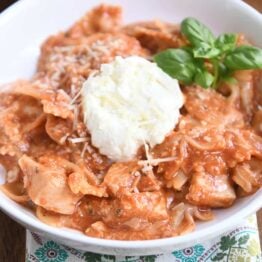 serving of chicken lasagna in white bowl with spoonful of ricotta and fresh basil leaves