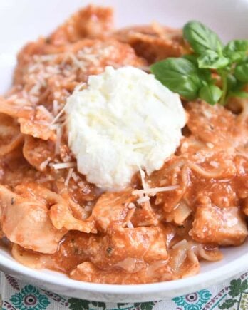 serving of chicken lasagna in white bowl with spoonful of ricotta and fresh basil leaves