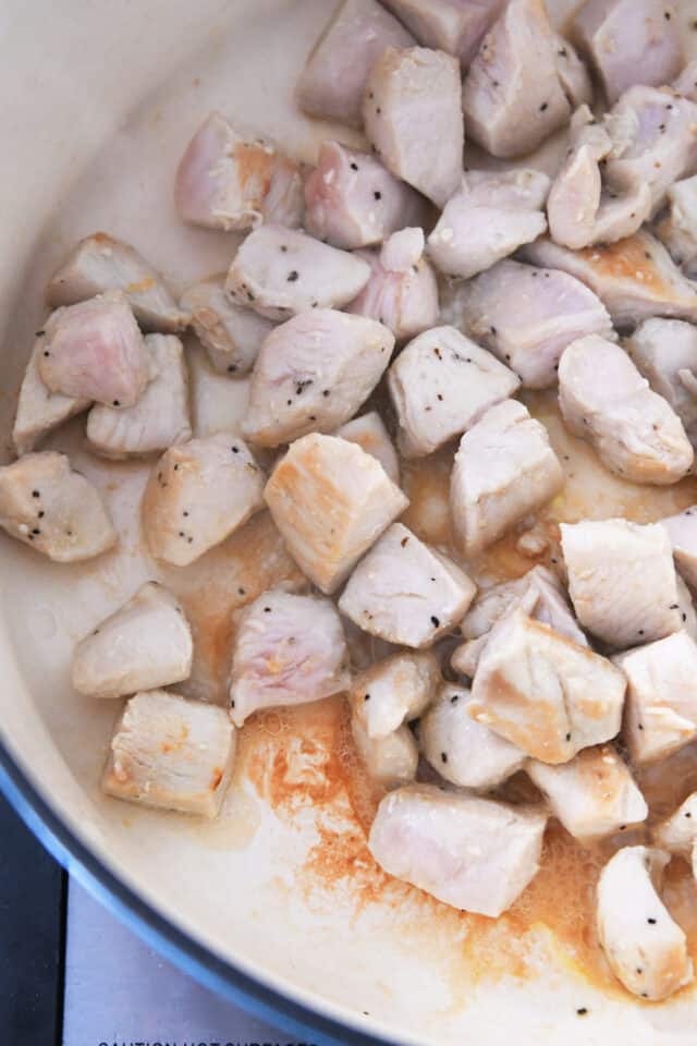 Chicken cubes cooking in oil in cast iron pot.