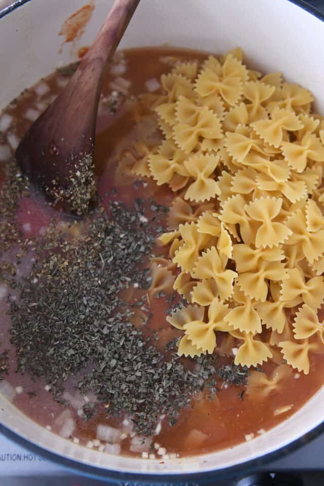 bowtie pasta, broth, oregano basil in cast iron pot