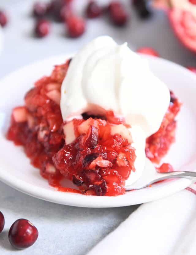 Spoon scooping bite of cranberry pomegranate jello salad on white plate.