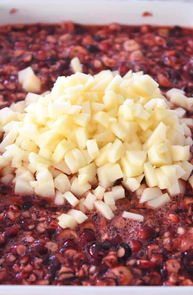 Diced apples in dish with pomegranate arils, cranberries, jello and sugar.