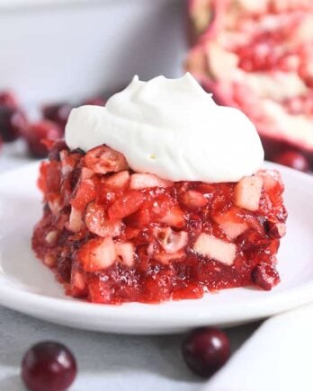 square of cranberry pomegranate jello salad on white plate with whipped topping