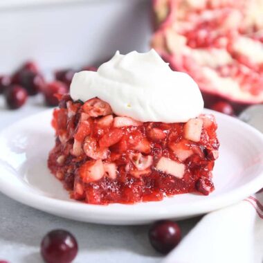 square of cranberry pomegranate jello salad on white plate with whipped topping