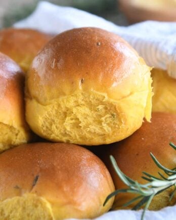 basket of several pumpkin dinner rolls with spring of fresh rosemary