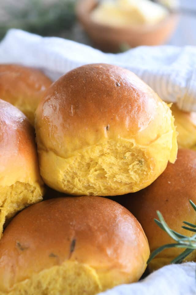 Basket of pumpkin dinner rolls with white towel.