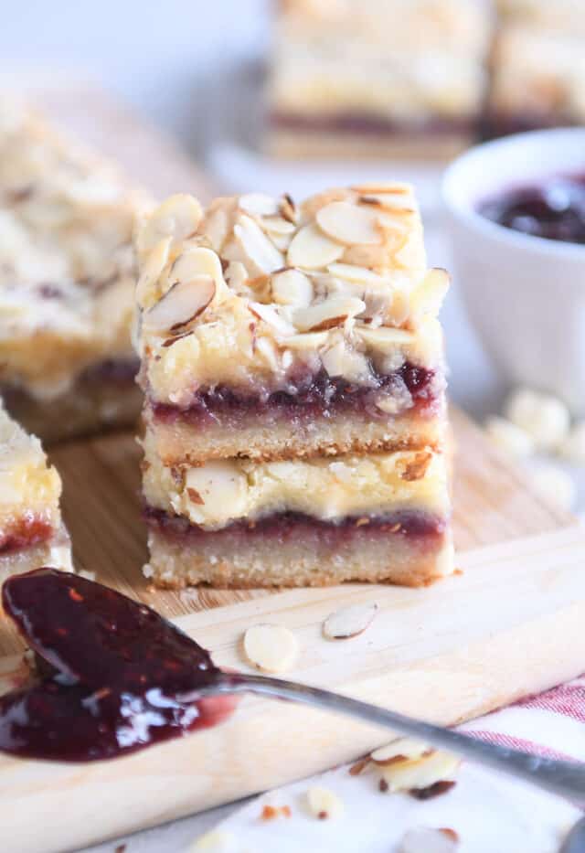 two raspberry white chocolate blondie bars stacked on each other on wood cutting board with spoon of raspberry jam
