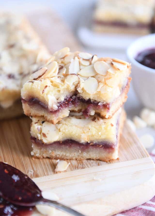 Two raspberry white chocolate blondie bars on wood cutting board with bite taken out of top bar.