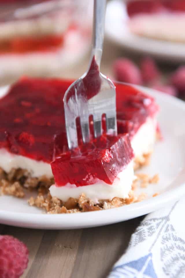 Fork scooping off corner of raspberry pretzel jello on white plate.