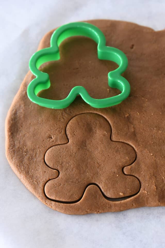 Cutting out gingerbread people with green cookie cutter.