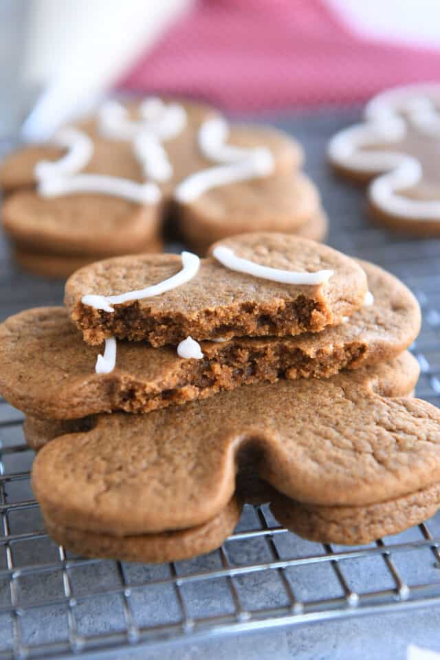 Soft and chewy gingerbread cookie broken in half and stacked on two other gingerbread people on wire rack.